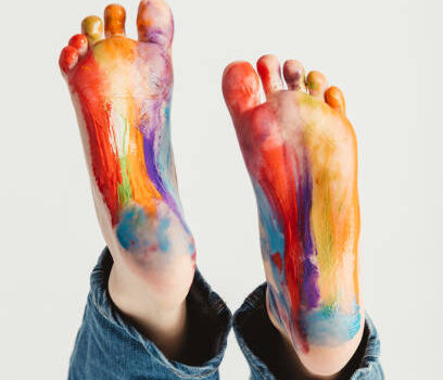 Kid's feet painted in rainbow colors with acrylic paint.